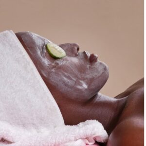 A relaxed woman, lying down whilst wearing a face mask, she has cucumbers on her eyes and a towel around her hair